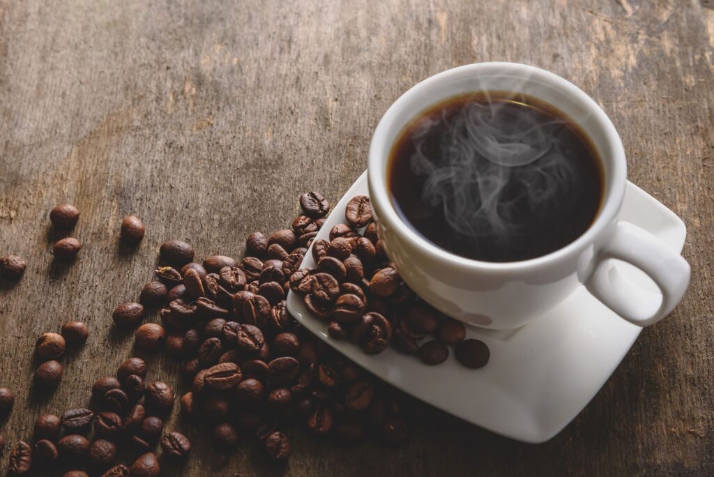 White cup and saucer full of coffee on table next to coffee beans